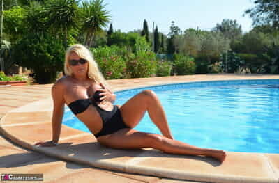 Middle-aged blonde Sweet Susi frees her tits & pussy from a swimsuit by a pool