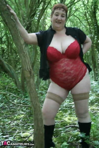 Mature lady Kinky Carol shows her huge tits and butt amid undergrowth