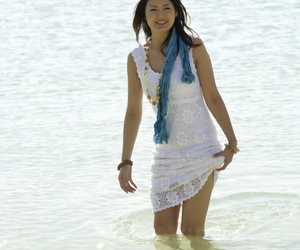 Asian girl wander into the ocean to her knees in a white dress