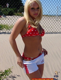 Blond adolescent Kathy Ash dolls a polka-dot bikini against a fence at the beach