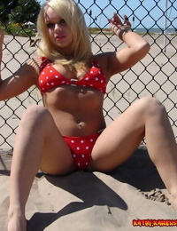Blond infant Kathy Ash girls a polka-dot bikini against a fence at the beach