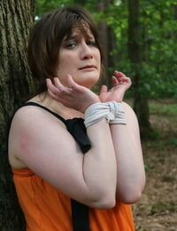 Fat female is gagged and tied to a tree in the woods with her clothes on