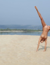 Agile fairy-haired Afina meditating naked and stretching on the beach