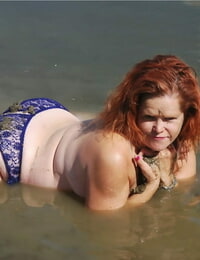 Redheaded amateur Misha covers her big tits in mud while in shallow water