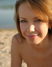 Slim teenage with crimson hair and a pretty face models fully nude on beach sand