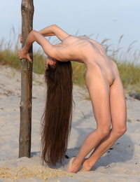 Supple teenager Lola G climbs a pillar on the beach while completely nude