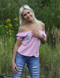 Blonde teen uncovers her small tits and bare ass next to a log in the country