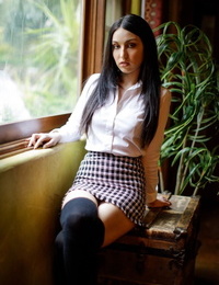 Dark haired girl peels off to seized over the knee socks in front of a window