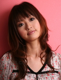 Japanese model with a pretty face stands clothed against a pink wall