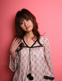 Japanese model with a pretty face stands clothed against a pink wall